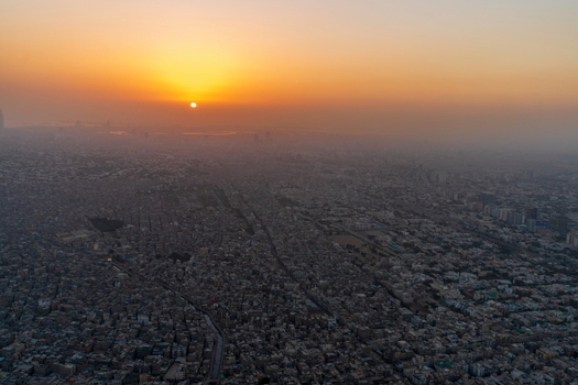 Aerial view of the sprawling urban landscape at sunset with dense residential buildings stretching to the horizon under a golden hazy sky in Karachi Sindh Pakistan.