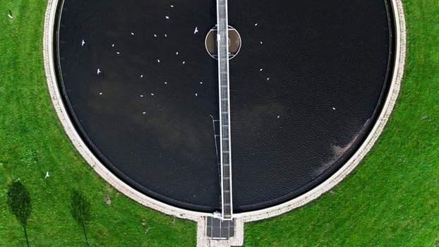 Aerial view of a circular wastewater treatment tank surrounded by green grass with a metal bridge structure crossing the dark water in Warmenhuizen North Holland Netherlands. Aerial view of a circular wastewater treatment tank surrounded by green grass with a metal bridge structure crossing the dark water in Warmenhuizen North Holland Netherlands.