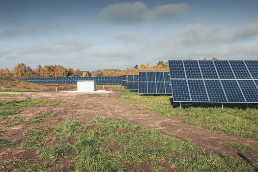 View of solar panels in a field with autumn trees in the background under a blue sky in Tartu County Estonia. View of solar panels in a field with autumn trees in the background under a blue sky in Tartu County Estonia.