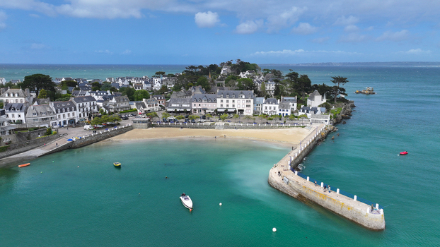 Aerial view of the coastal town of Locquirec featuring a sandy beach stone pier and traditional houses overlooking turquoise waters in Locquirec Brittany France. Aerial view of the coastal town of Locquirec featuring a sandy beach stone pier and traditional houses overlooking turquoise waters in Locquirec Brittany France.