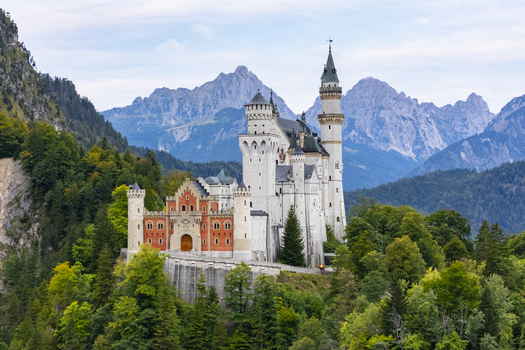 Aerial view of Neuschwanstein Castle amidst lush forests and towering mountains a fairytale fortress of stone and dreams Fussen Bayern Germany. Aerial view of Neuschwanstein Castle amidst lush forests and towering mountains a fairytale fortress of stone and dreams Fussen Bayern Germany.