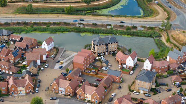 Aerial view of a modern residential housing estate featuring brick houses with tiled roofs a small pond and parked cars in Bedford England United Kingdom. Aerial view of a modern residential housing estate featuring brick houses with tiled roofs a small pond and parked cars in Bedford England United Kingdom.