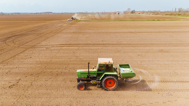 Aerial view of a green tractor spreading fertilizer across the vast dry ploughed fields under a pastel sky Sremska Mitrovica Vojvodina Serbia. Aerial view of a green tractor spreading fertilizer across the vast dry ploughed fields under a pastel sky Sremska Mitrovica Vojvodina Serbia.