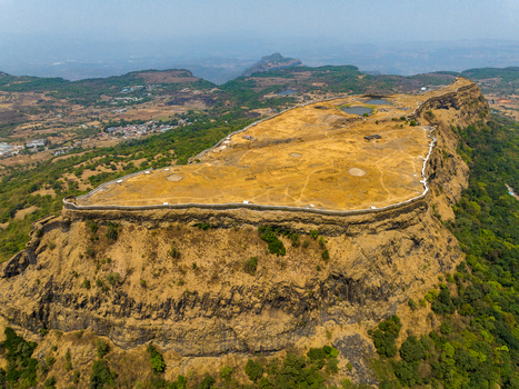 Aerial view of Korigad Fort a historic hill fort with stone ramparts and dry grassy plateau surrounded by lush green forests and rolling hills in Peth Shahapur Maharashtra India. Aerial view of Korigad Fort a historic hill fort with stone ramparts and dry grassy plateau surrounded by lush green forests and rolling hills in Peth Shahapur Maharashtra India.