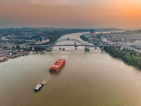 Aerial view of Jembatan Mahakam I with a tugboat pulling a barge along the Mahakam River at sunset in Kecamatan Samarinda Seberang Kalimantan Timur Indonesia. Aerial view of Jembatan Mahakam I with a tugboat pulling a barge along the Mahakam River at sunset in Kecamatan Samarinda Seberang Kalimantan Timur Indonesia.