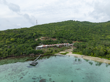 Aerial view of a tranquil beachside resort nestled against a lush green hillside where the turquoise waters meet the soft sandy shore at Cottage Legon Waru Karimunjawa Indonesia.