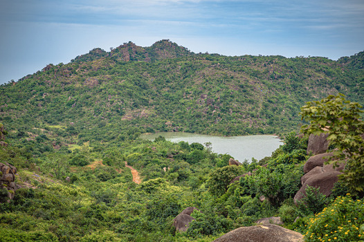 View of Lamingo Dam surrounded by rocky hills and lush green vegetation under a cloudy sky in Jos Plateau Nigeria.