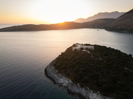 Aerial view of Porto Palermo Castle on a lush peninsula overlooking the calm Ionian Sea during a golden sunset with mountains in the distance Himare Vlore County Albania. Aerial view of Porto Palermo Castle on a lush peninsula overlooking the calm Ionian Sea during a golden sunset with mountains in the distance Himare Vlore County Albania.