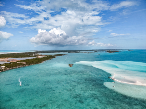 Aerial view of the Man O War Cay Sandbar surrounded by turquoise waters small boats and lush tropical coastline under a cloudy sky in Rolletown Exuma The Bahamas. Aerial view of the Man O War Cay Sandbar surrounded by turquoise waters small boats and lush tropical coastline under a cloudy sky in Rolletown Exuma The Bahamas.