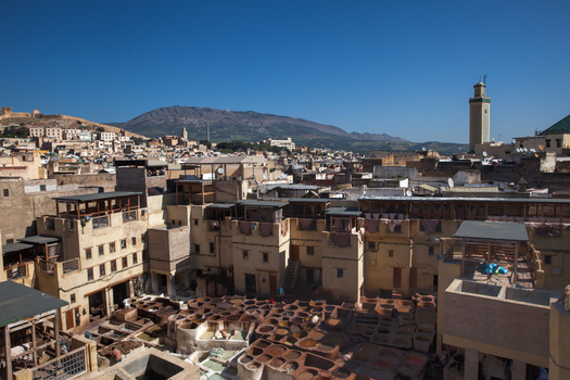 View of the historic Chouara Tannery with stone vats filled with colorful dyes workers and surrounding traditional buildings under a clear blue sky in Morocco.
