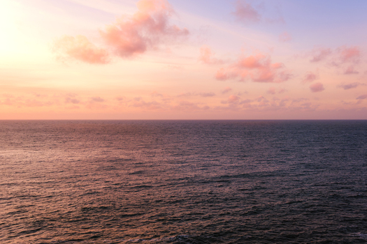 View of the Atlantic Ocean with soft waves under a sky filled with pink and orange clouds during sunset in Hayle Cornwall United Kingdom.