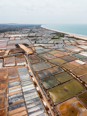 Aerial view of expansive salt production fields with geometric patterns and varying water levels along the coastline of Vietnam. Aerial view of expansive salt production fields with geometric patterns and varying water levels along the coastline of Vietnam.