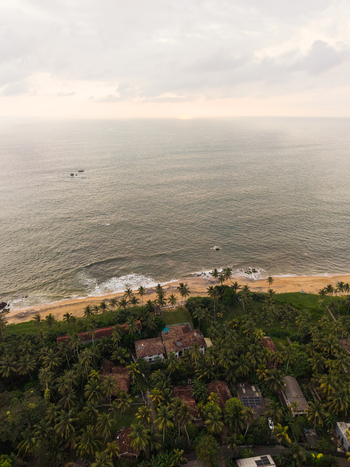 Aerial view of a tropical coastline with palm trees luxury villas and ocean waves under a soft sunset sky in Galle Southern Province Sri Lanka.
