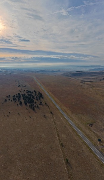 Aerial view of a highway stretching through the vast dry landscape with sparse trees and distant mountains in Golden Colorado United States.