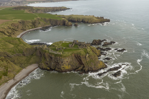 Aerial view of Dunnottar Castle perched on a rugged cliff overlooking the North Sea with green fields and rocky coastline Stonehaven Scotland United Kingdom. Aerial view of Dunnottar Castle perched on a rugged cliff overlooking the North Sea with green fields and rocky coastline Stonehaven Scotland United Kingdom.