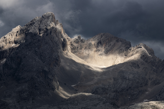 View of the rugged peaks of the Dolomites with dramatic sunlight illuminating the rocky slopes under dark storm clouds Trentino Alto Adige Italy. View of the rugged peaks of the Dolomites with dramatic sunlight illuminating the rocky slopes under dark storm clouds Trentino Alto Adige Italy.