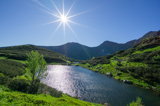 View of Rohacske plesa mountain lake surrounded by green slopes and rocky peaks under a bright sun in Zuberec Zilina Region Slovakia. View of Rohacske plesa mountain lake surrounded by green slopes and rocky peaks under a bright sun in Zuberec Zilina Region Slovakia.