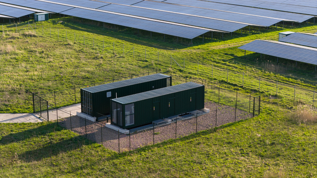 Aerial view of a solar farm featuring rows of photovoltaic panels and green battery storage containers within a fenced enclosure in Farmsum Groningen Netherlands.