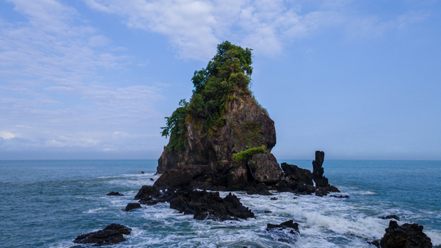 Aerial view of Pantai Karang Agung a large rock formation covered in green vegetation rising from the sea with waves crashing against its base Ayah Central Java Indonesia. Aerial view of Pantai Karang Agung a large rock formation covered in green vegetation rising from the sea with waves crashing against its base Ayah Central Java Indonesia.