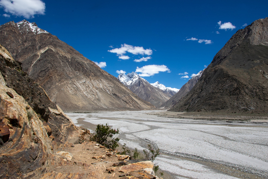 View of the rugged mountain landscape near K2 Base Camp with a wide rocky riverbed steep slopes and clear blue sky in Ghakhar Gilgit Pakistan. View of the rugged mountain landscape near K2 Base Camp with a wide rocky riverbed steep slopes and clear blue sky in Ghakhar Gilgit Pakistan.