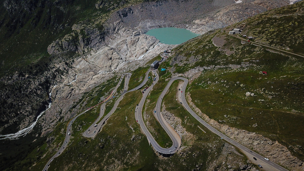 Aerial view of the winding Furka Pass road near the Rhone Glacier lake and rugged alpine peaks in Obergoms Valais Switzerland. Aerial view of the winding Furka Pass road near the Rhone Glacier lake and rugged alpine peaks in Obergoms Valais Switzerland.