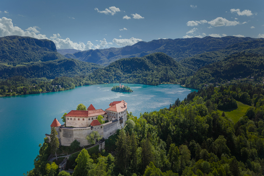 Aerial view of Bled Castle on a cliff overlooking the turquoise waters of Lake Bled with the island church and Julian Alps in Bled Radovljica Slovenia.