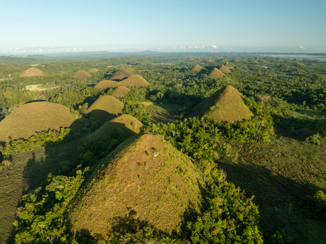 Aerial view of the Chocolate Hills a landscape of conical limestone hills covered in grass and lush vegetation under soft sunlight in Batuan Central Visayas Philippines. Aerial view of the Chocolate Hills a landscape of conical limestone hills covered in grass and lush vegetation under soft sunlight in Batuan Central Visayas Philippines.