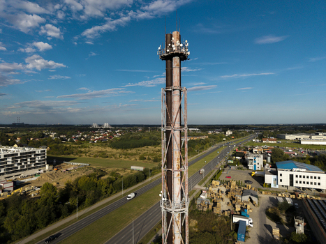 Aerial view of a tall industrial chimney equipped with communication antennas rising above a highway and surrounding urban landscape in Krakow Lesser Poland Voivode Poland.