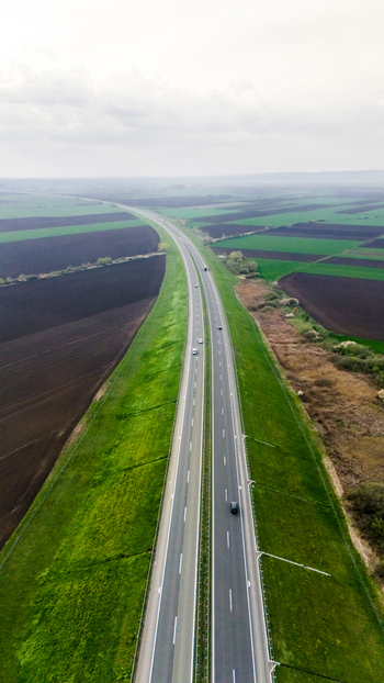 Aerial view of a modern highway slicing through a vibrant tapestry of green fields and dark earth under a soft overcast sky Sremska Mitrovica Vojvodina Serbia. Aerial view of a modern highway slicing through a vibrant tapestry of green fields and dark earth under a soft overcast sky Sremska Mitrovica Vojvodina Serbia.