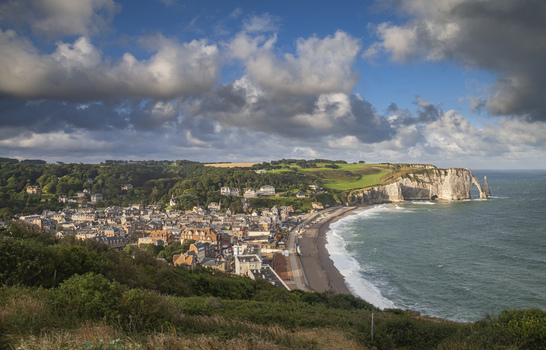 Aerial view of the dramatic cliffs meeting the sea with a charming town nestled below under a sky streaked with clouds &Eacute;tretat France.
