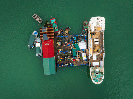 Aerial view of a floating platform with solar panels surrounded by small boats and fishing vessels in the green water of Vietnam. Aerial view of a floating platform with solar panels surrounded by small boats and fishing vessels in the green water of Vietnam.