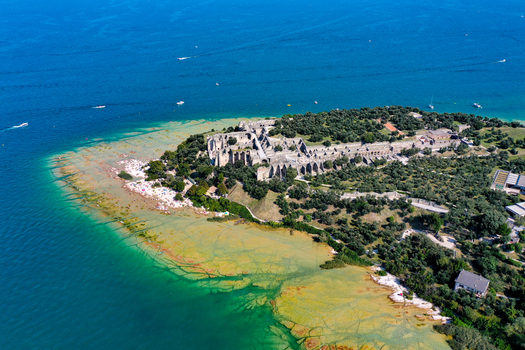 Aerial view of the Grotte di Catullo ancient Roman ruins and a crowded beach on the tip of the peninsula by the turquoise waters of Lake Garda Sirmione Lombardia Italy. Aerial view of the Grotte di Catullo ancient Roman ruins and a crowded beach on the tip of the peninsula by the turquoise waters of Lake Garda Sirmione Lombardia Italy.