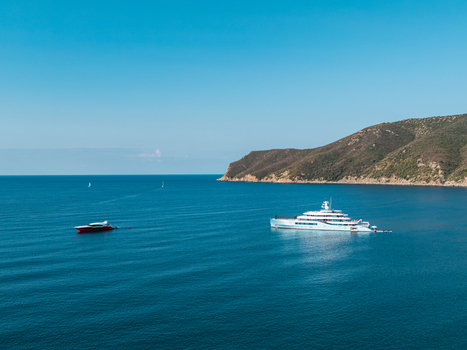 Aerial view of the luxury yacht Netto II anchored in the blue waters of Lacona Bay on Elba with a smaller red boat nearby and green hills in the background Lacona Tuscany Italy.