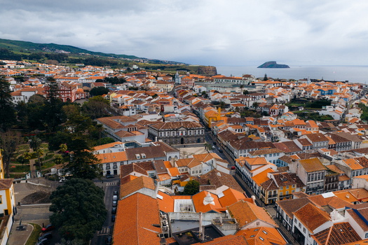 Aerial view of the historic city center with orange tiled rooftops traditional architecture and the Atlantic Ocean under a cloudy sky in Angra do Heroismo Azores Portugal.