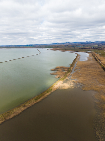 Aerial view of Lake Atanasovsko with calm waters dry reeds along the shoreline and rolling hills under a cloudy sky in Burgas Burgas Bulgaria. Aerial view of Lake Atanasovsko with calm waters dry reeds along the shoreline and rolling hills under a cloudy sky in Burgas Burgas Bulgaria.