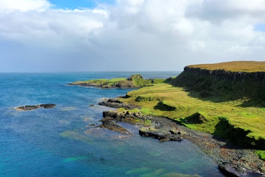 Aerial view of The Brother s Point featuring dramatic coastal cliffs lush green grassy slopes and rocky shoreline meeting the blue sea in Culnacnoc Scotland United Kingdom. Aerial view of The Brother s Point featuring dramatic coastal cliffs lush green grassy slopes and rocky shoreline meeting the blue sea in Culnacnoc Scotland United Kingdom.