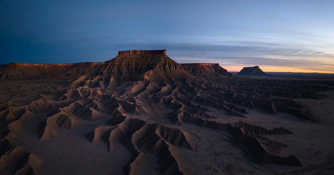 Aerial view of the dramatic eroded badlands and buttes near Caineville at golden hour with long shadows stretching across the desert landscape in Caineville Utah United States. Aerial view of the dramatic eroded badlands and buttes near Caineville at golden hour with long shadows stretching across the desert landscape in Caineville Utah United States.
