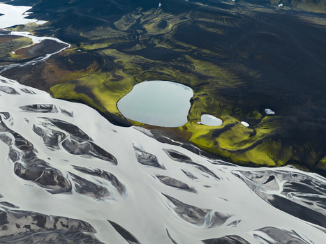 Aerial view of glacial rivers carving through black volcanic earth juxtaposed with bright green moss and still lakes Highlands Iceland.