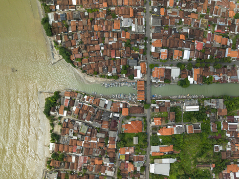 Aerial view of terracotta rooftops meet the murky waters at the Jepara Floating Fish Market contrasting with the boats docked along the river Jepara Central Java Indonesia.