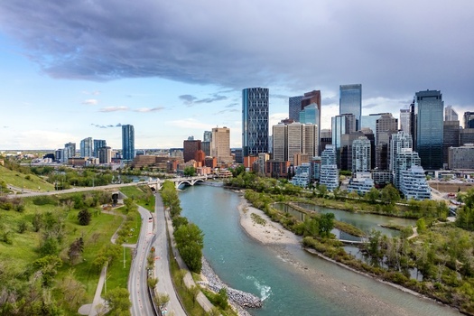 Aerial view of the Calgary skyline featuring modern skyscrapers the Bow River and lush green parklands under a dramatic cloudy sky in Calgary Alberta Canada.