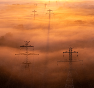 Aerial view of transmission towers rising through thick golden morning fog at sunrise in Bridgman Michigan United States.