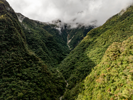 Aerial view of the Urubamba River winding through a lush jungle valley surrounded by steep vegetation covered mountains under a cloudy sky in Aguas Calientes Cusco Peru. Aerial view of the Urubamba River winding through a lush jungle valley surrounded by steep vegetation covered mountains under a cloudy sky in Aguas Calientes Cusco Peru.