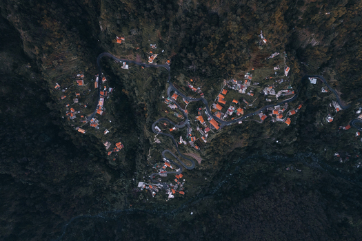 Aerial view of Curral das Freiras village nestled in a deep mountain valley with winding roads and orange rooftops surrounded by dense forest in Curral das Freiras Madeira Portugal. Aerial view of Curral das Freiras village nestled in a deep mountain valley with winding roads and orange rooftops surrounded by dense forest in Curral das Freiras Madeira Portugal.