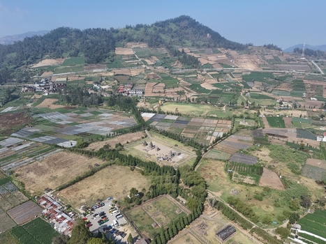 Aerial view of the ancient Arjuna Temple complex surrounded by lush agricultural fields and mountainous landscape in Kecamatan Batur Jawa Tengah Indonesia.
