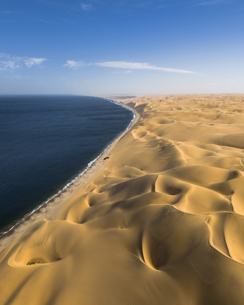 Aerial view of the dramatic meeting of the dark blue ocean and the endless ochre dunes a stark contrast of textures and tones creating a mesmerizing vista Anichab Erongo Namibia. Aerial view of the dramatic meeting of the dark blue ocean and the endless ochre dunes a stark contrast of textures and tones creating a mesmerizing vista Anichab Erongo Namibia.