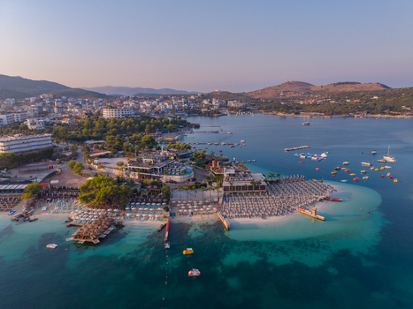 Aerial view of the coastal town of Ksamil with its turquoise waters sandy beaches rows of sun loungers and surrounding hills in Ksamil Vlore County Albania. Aerial view of the coastal town of Ksamil with its turquoise waters sandy beaches rows of sun loungers and surrounding hills in Ksamil Vlore County Albania.