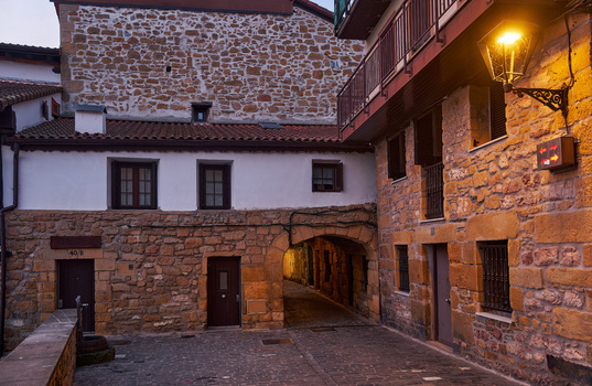 Pasai Donibane Spain 09 March 2026 View of the historic main harbor street with traditional stone buildings an arched passage and a glowing street lamp at dusk.