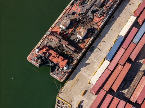 Aerial view of a weathered industrial barge docked at the port along the Rio Ozama with rows of shipping containers on the wharf in Santo Domingo Santo Domingo Dominican Republic.