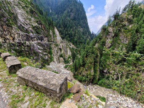 View of the rugged mountain landscape and deep river valley near the village featuring steep cliffs dense pine forests and stone road barriers in Malana Himachal Pradesh India.