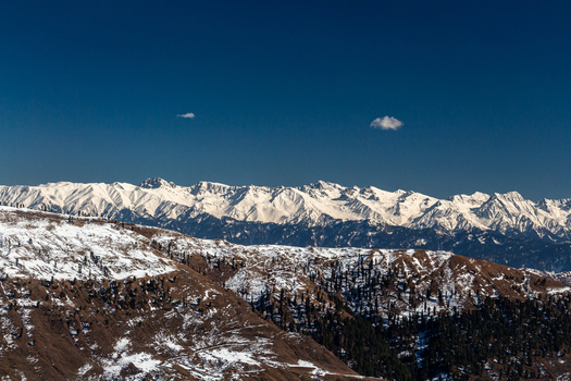 View of the rugged snow capped mountain range against the deep blue sky a serene contrast of cold whites and warm earth tones Lasdana Azad Kashmir Pakistan.